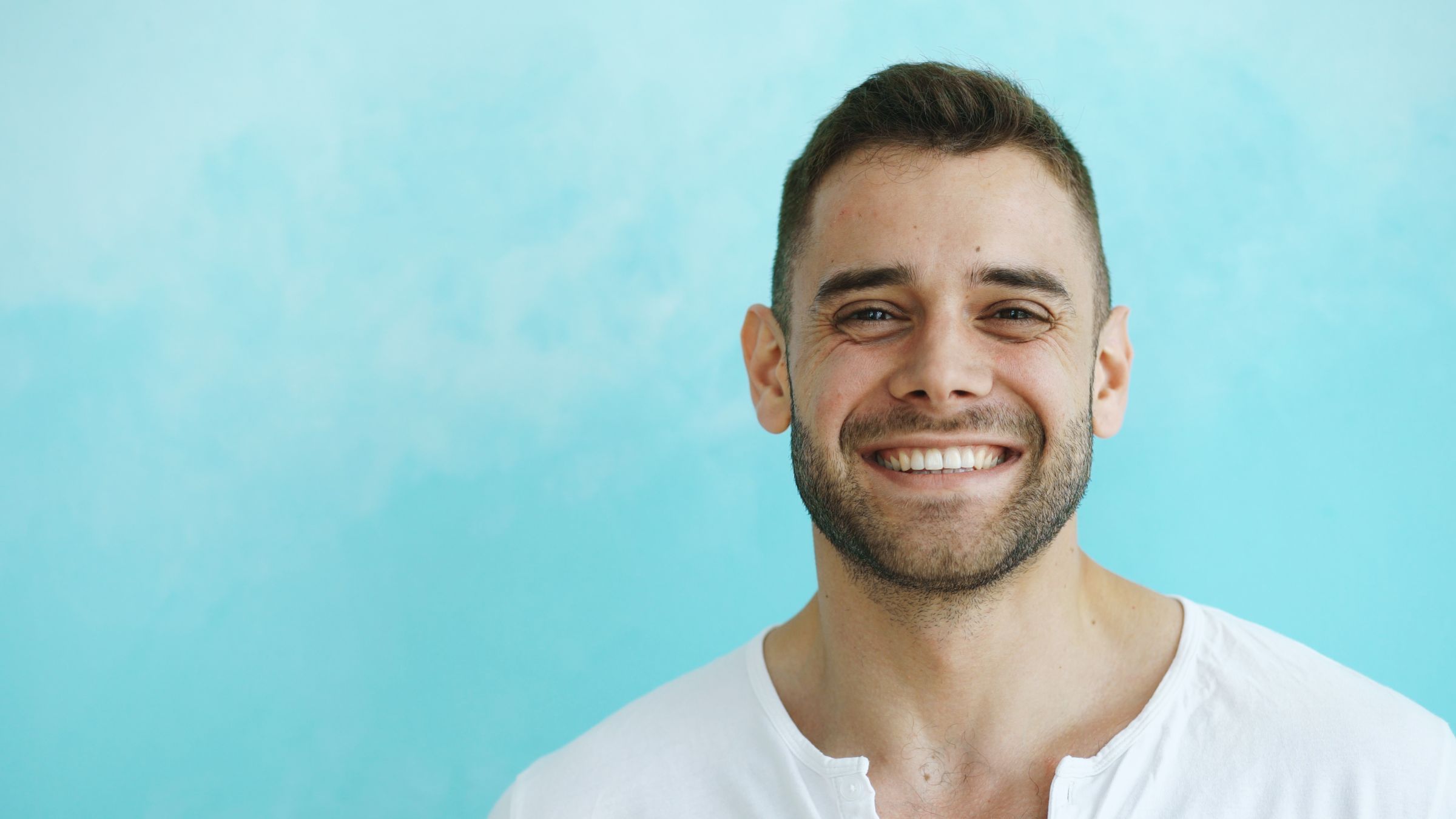Homem jovem a sorrir para a câmara sobre fundo azul, representando a consulta de PrEP online da EQUALcare